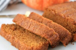 A loaf of fresh-milled pumpkin bread sliced with a pumpkin in the background