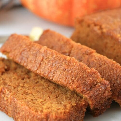 A loaf of fresh-milled pumpkin bread sliced with a pumpkin in the background