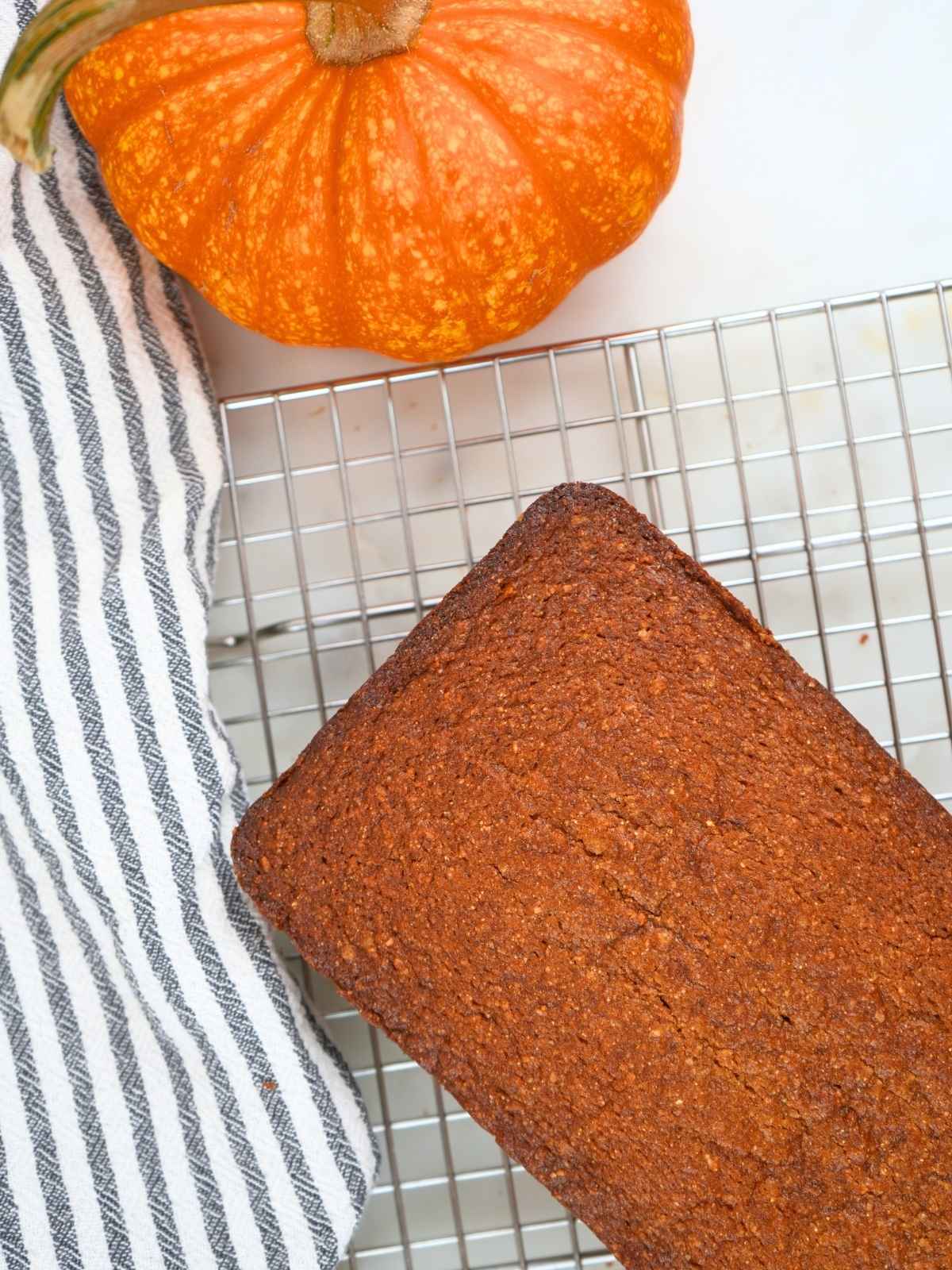 A loaf of fresh-milled pumpkin bread cooling on a wire rack.
