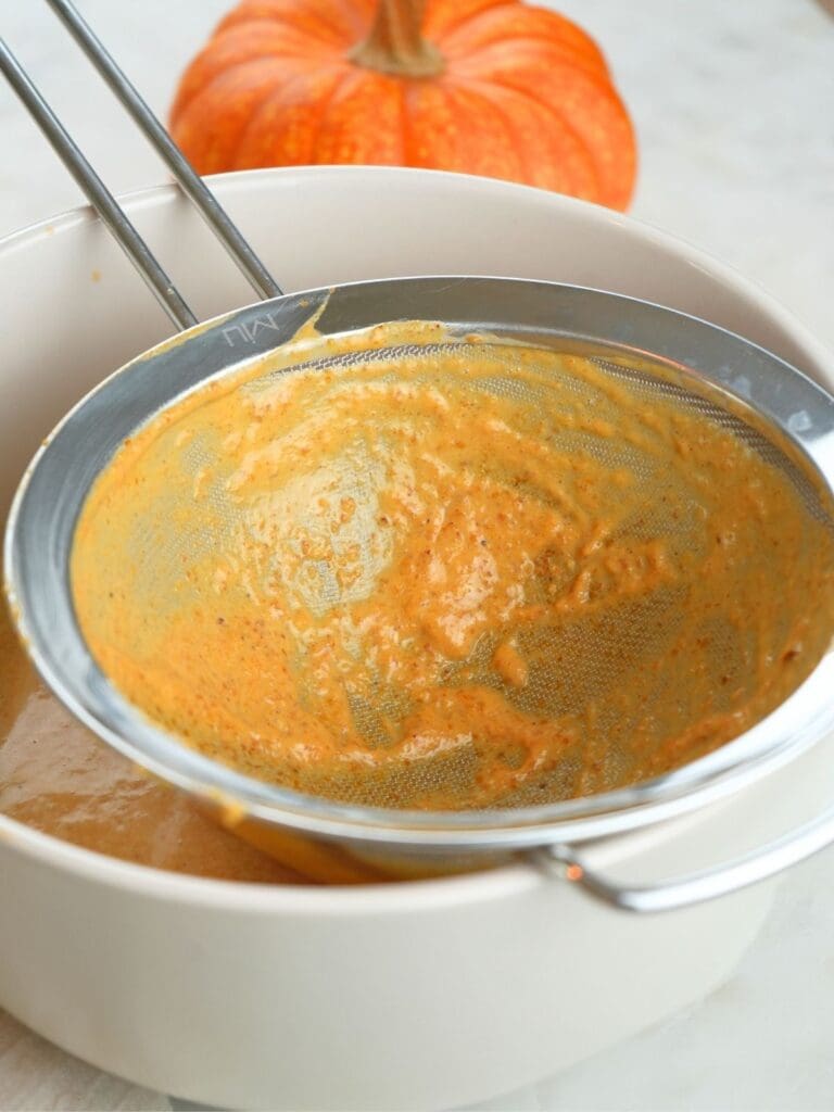 Pumpkin custard remnants in a mesh strainer over a bowl.