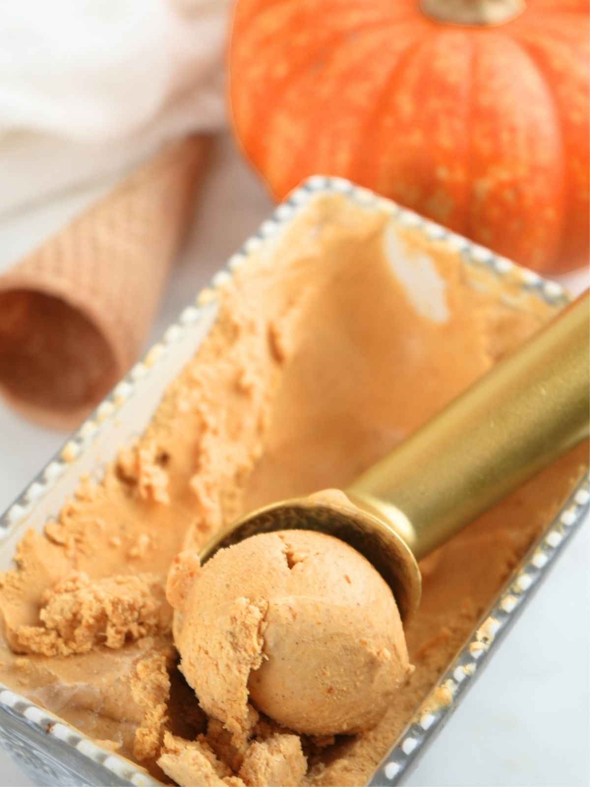 A container filled with homemade pumpkin ice cream and gold scoop.