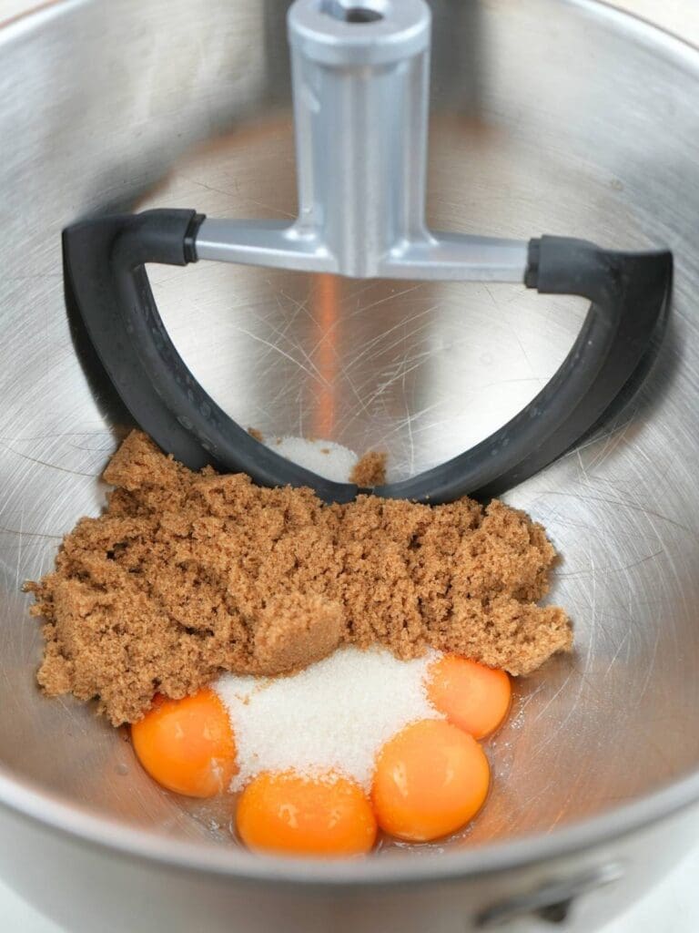 Egg yolks, granulated sugar, and brown sugar in a stand mixer bowl.