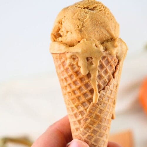 A close up of a scoop of homemade pumpkin ice cream on a sugar cone