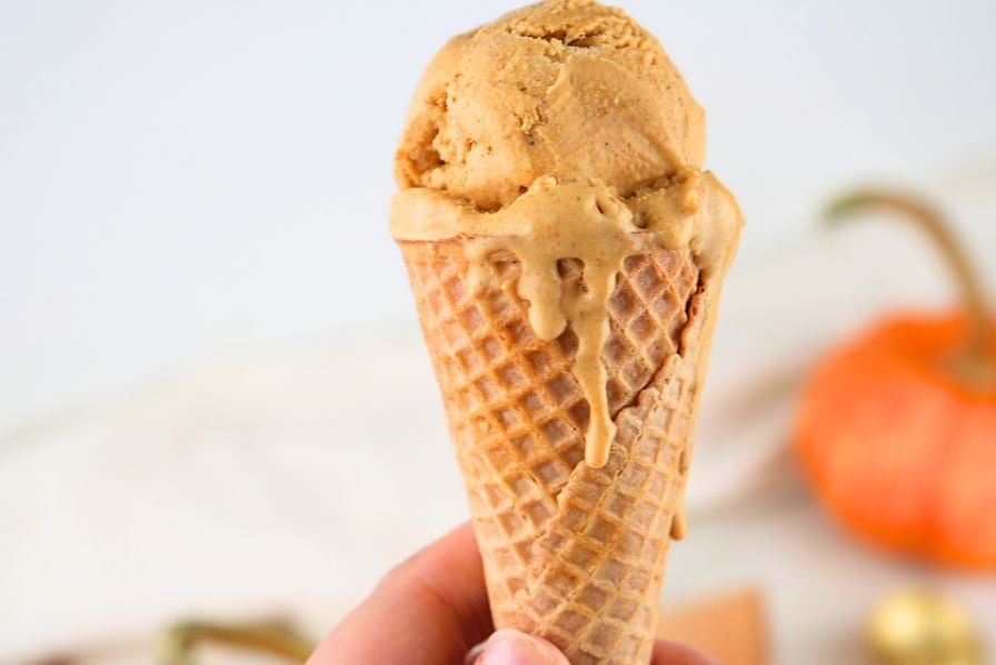 A close up of a scoop of homemade pumpkin ice cream on a sugar cone