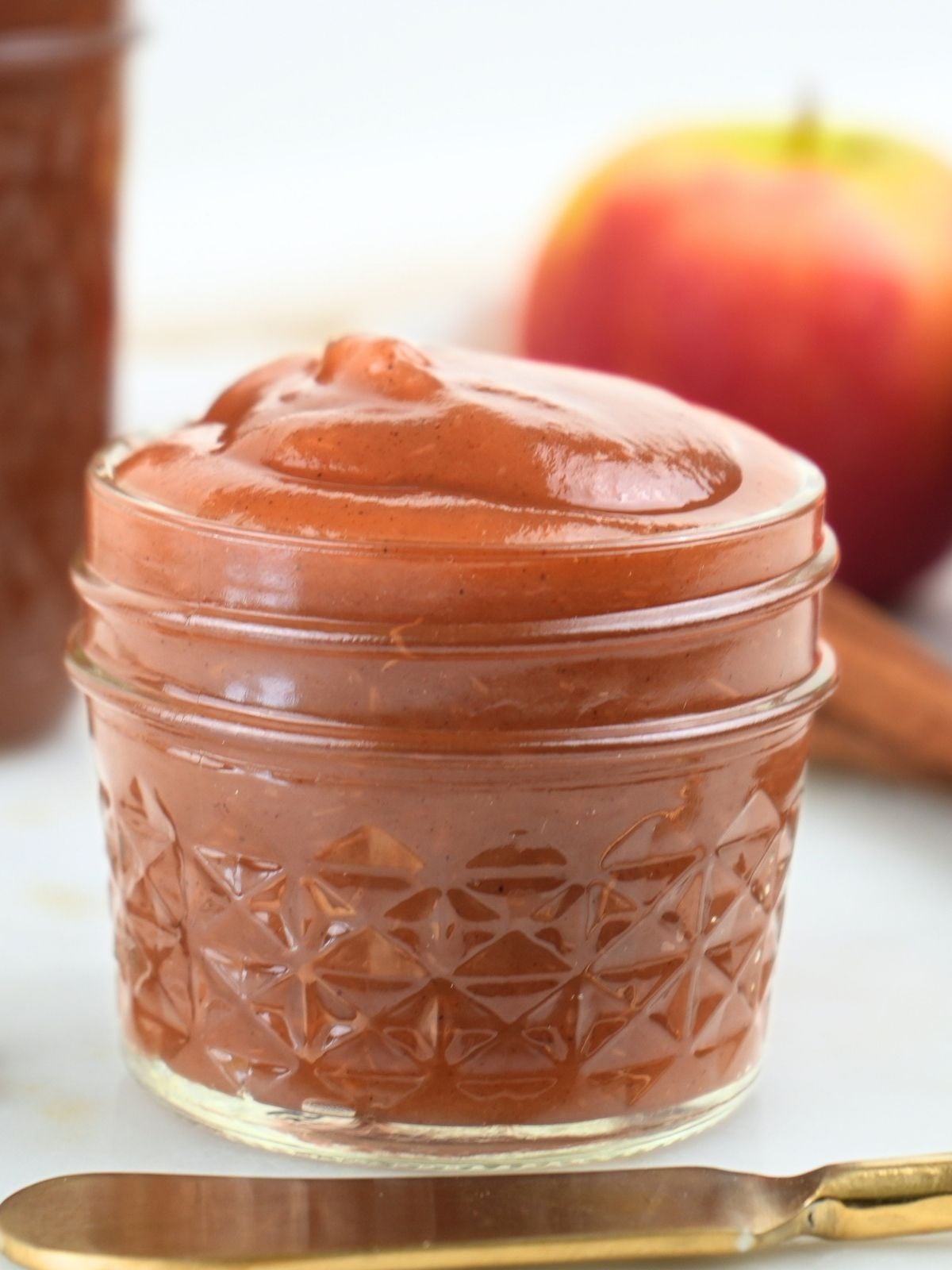 A jar of Instant Pot apple butter with a gold knife and a fresh apple.