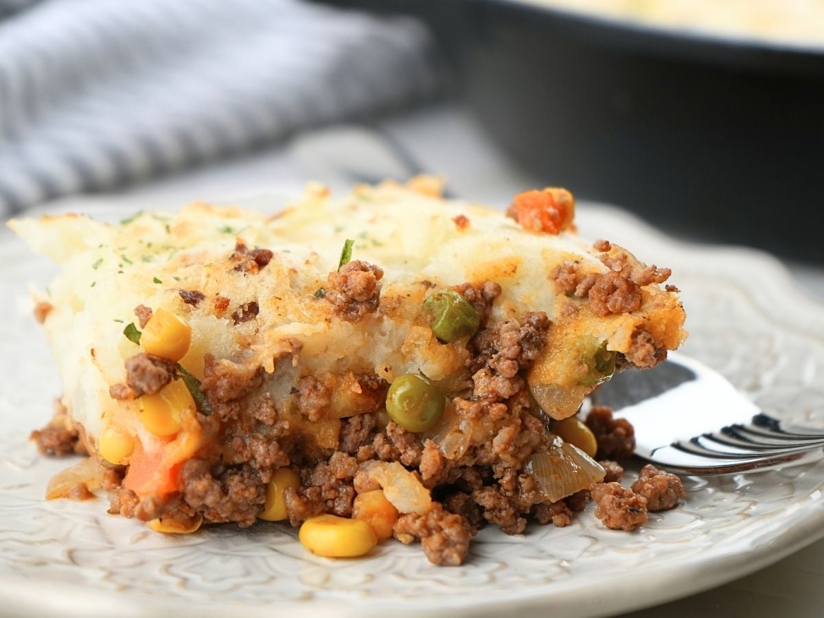 A scoop of shepherd's pie with corn on a plate with a fork.