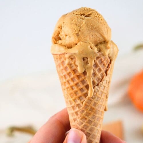 A hand holding pumpkin ice cream in a cone.