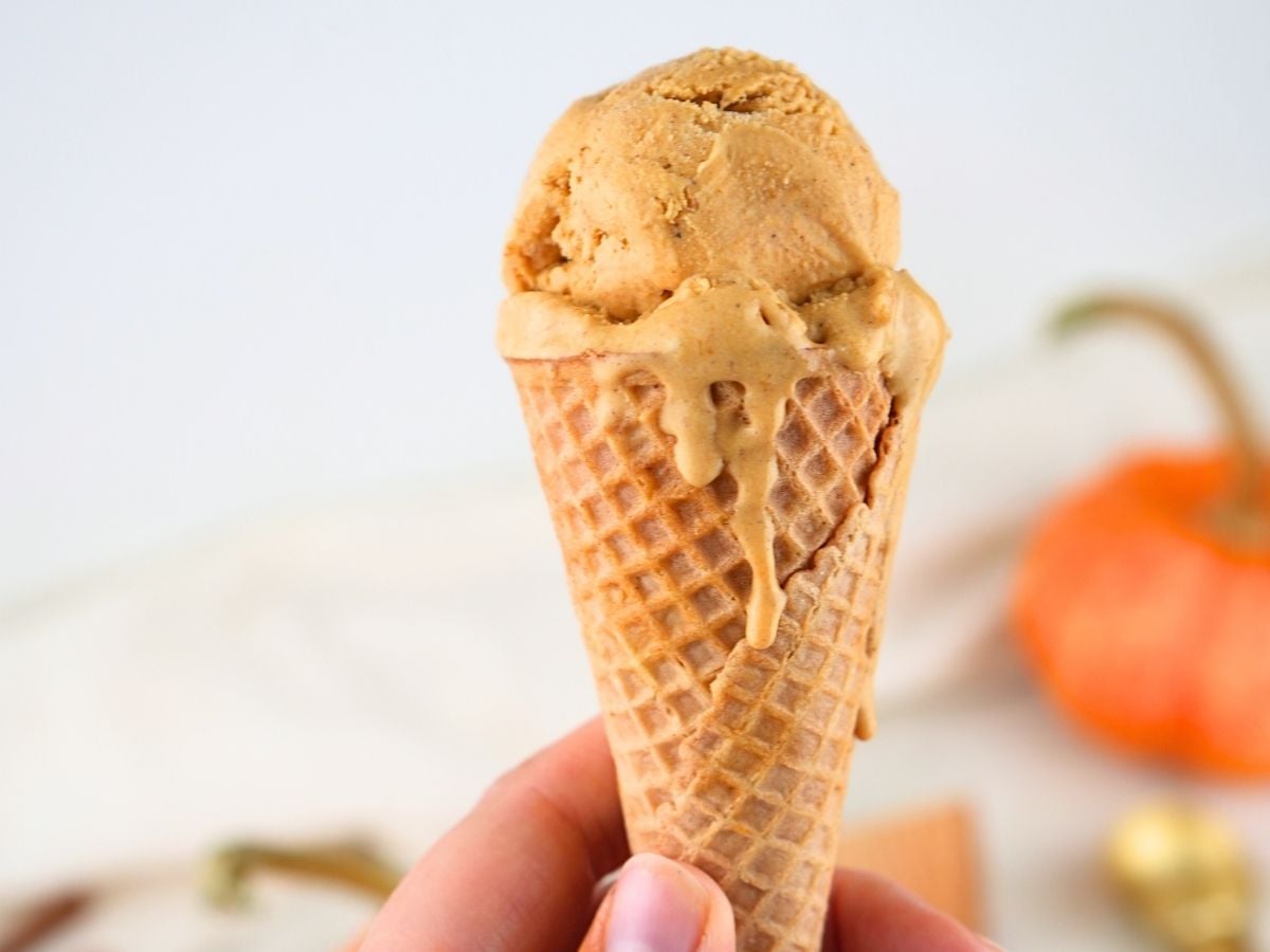 A hand holding pumpkin ice cream in a cone.