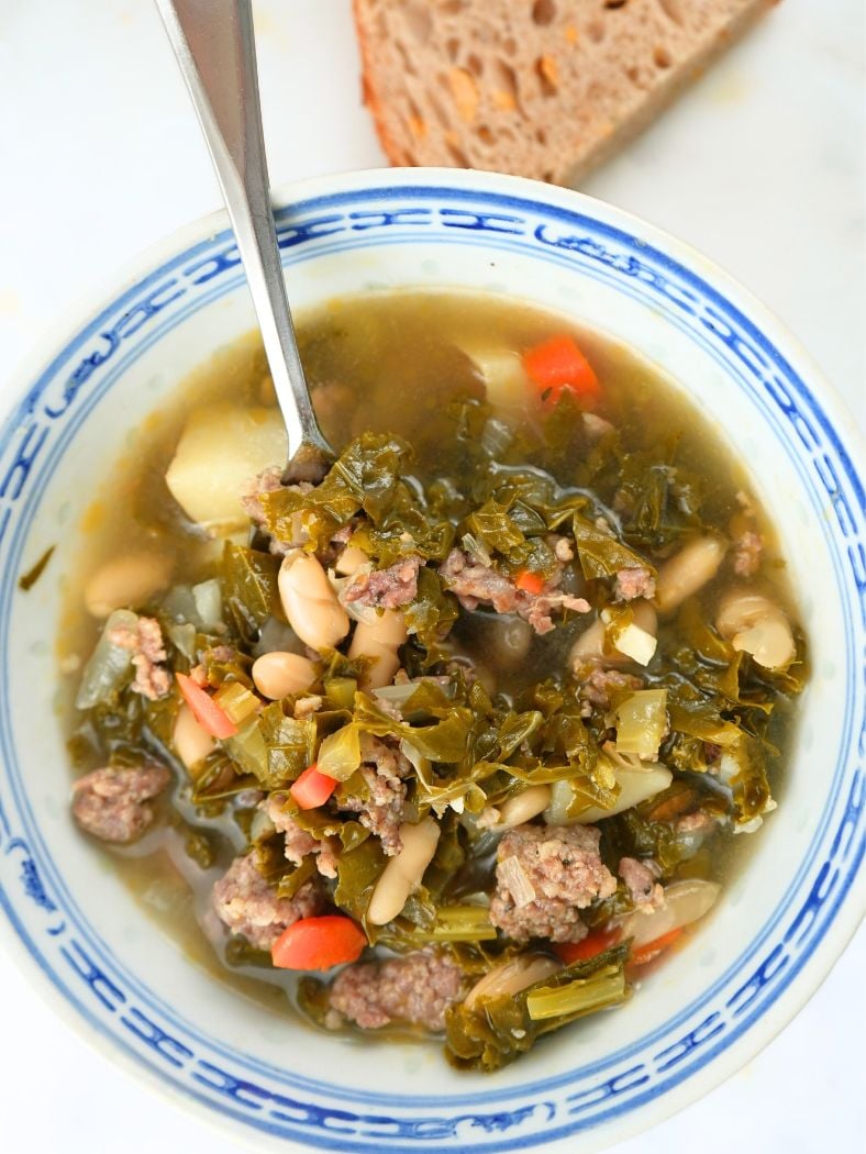 An overhead view of sausage, kale, and white bean soup with a spoon in it.