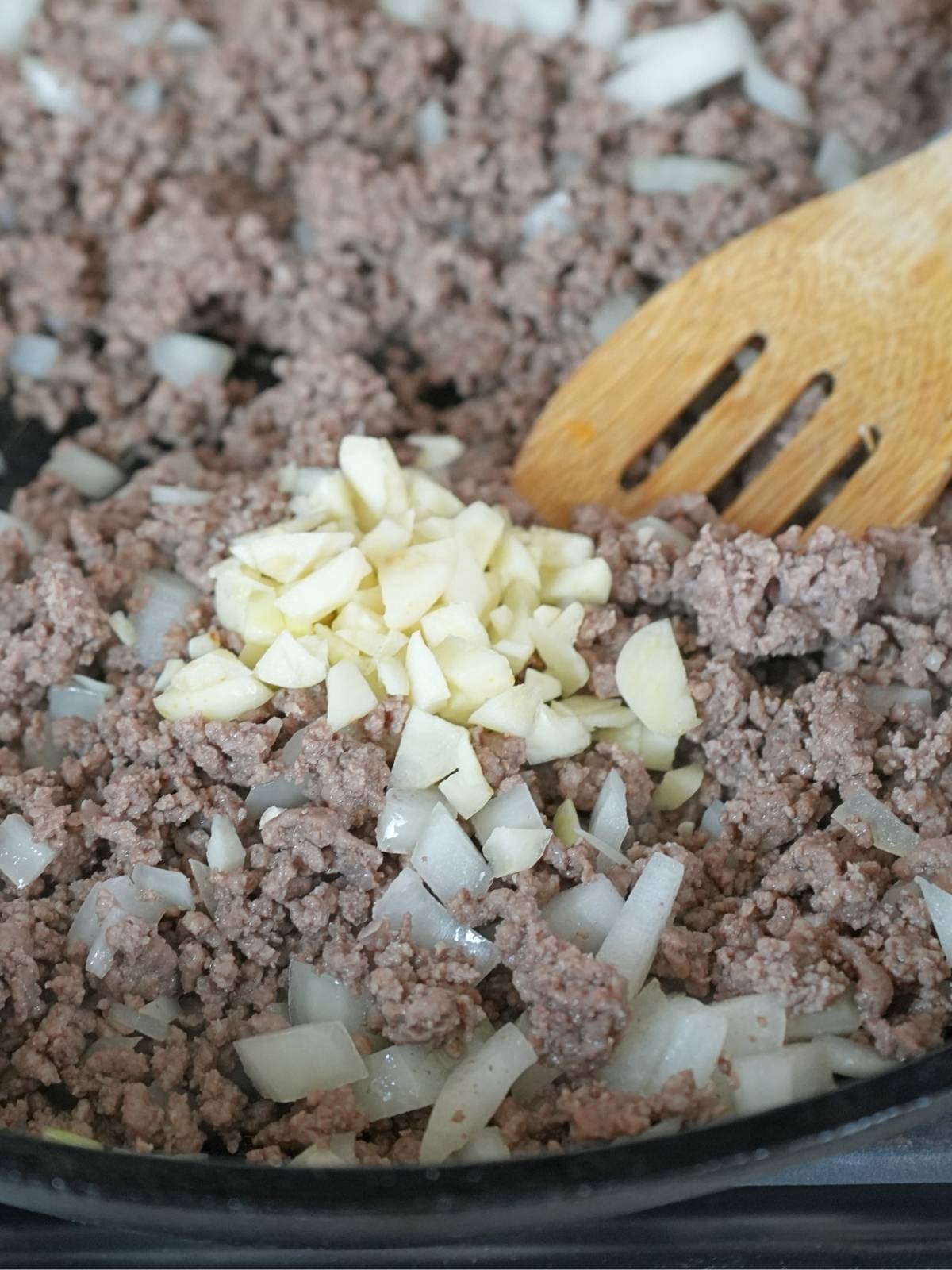 Ground beef and onions in a cast iron skillet topped with minced garlic.