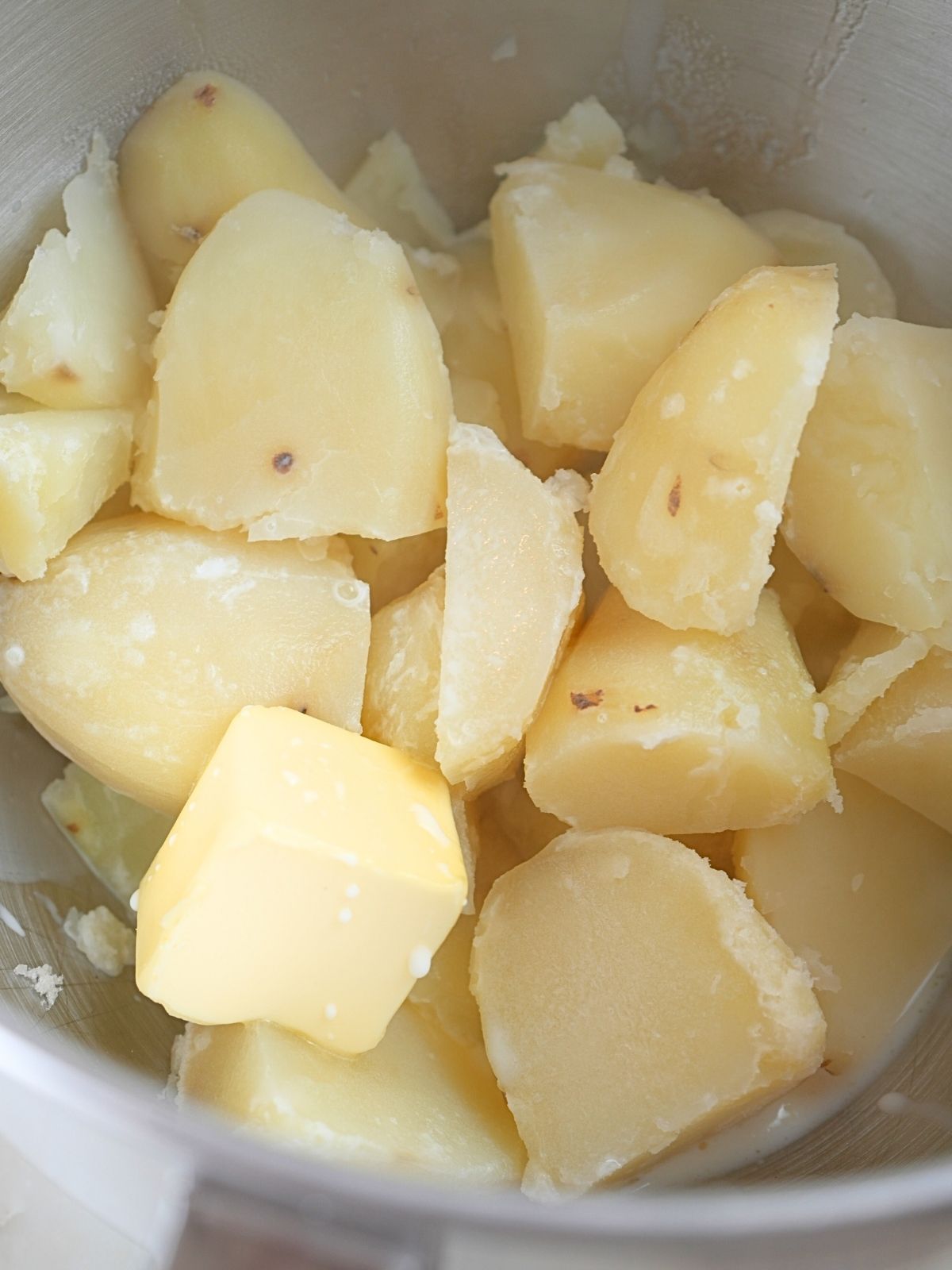 Cooked potatoes, butter, and milk in a mixing bowl