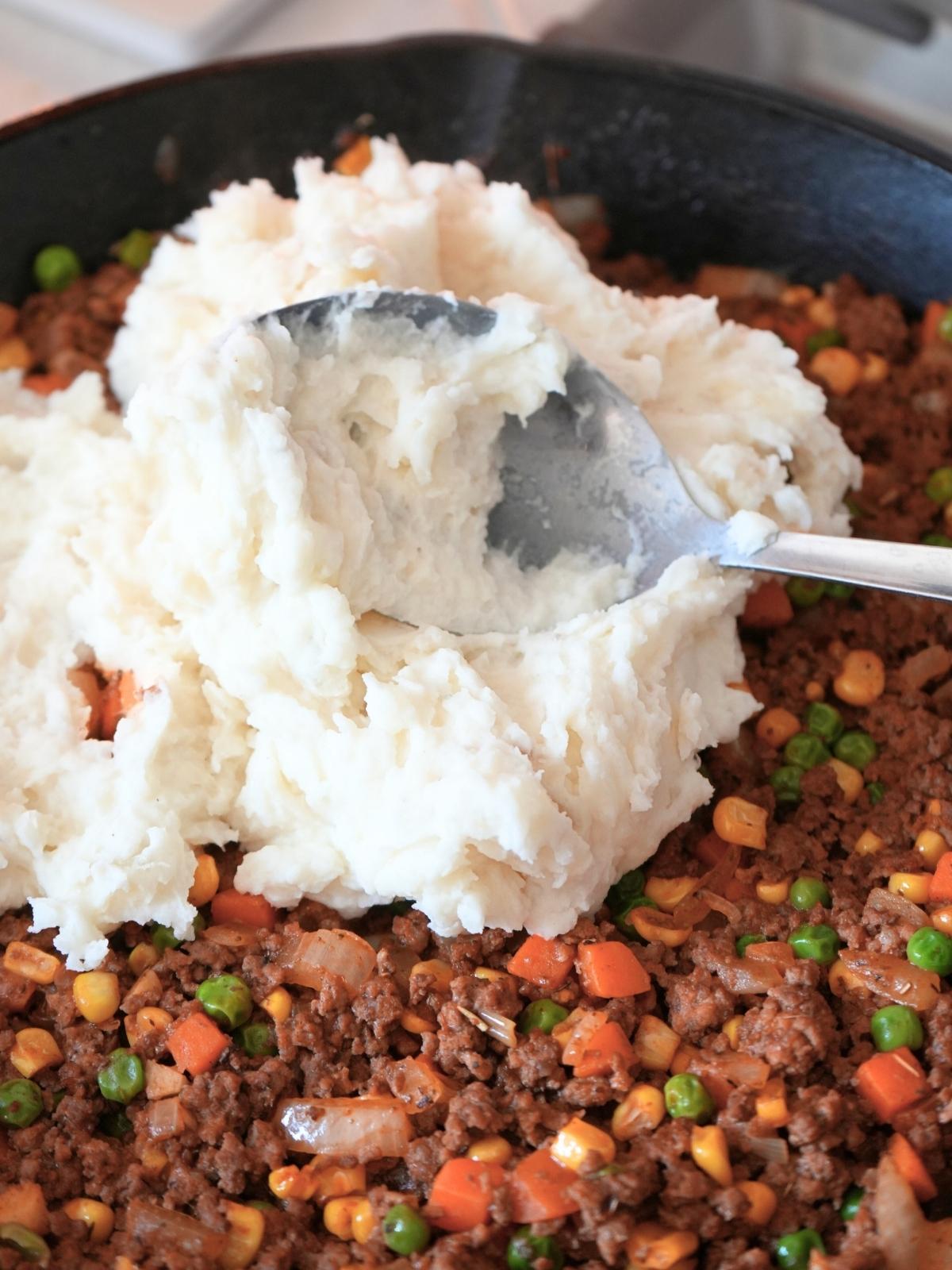 Mashed potatoes spooned over shepherd's pie with corn filling