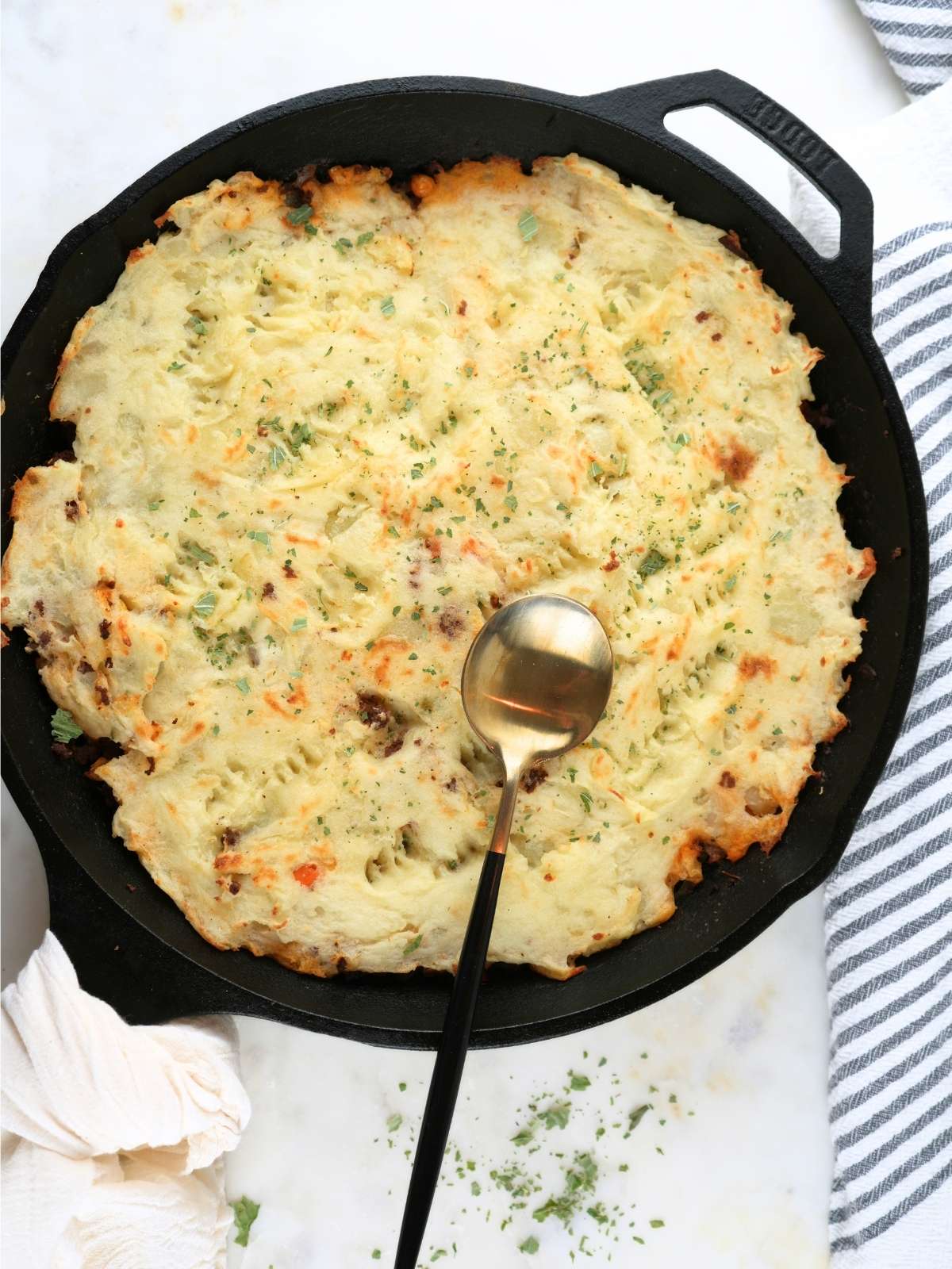 A finished shepherd's pie with corn, shown with decorative towels and a spoon.
