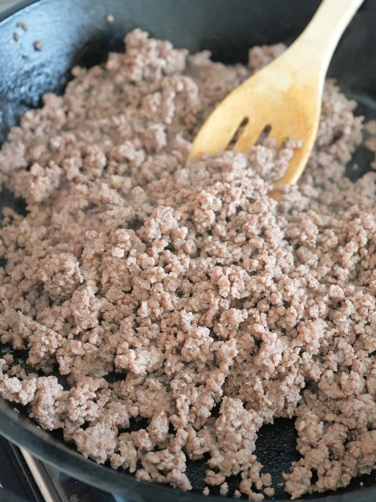 Ground beef browning in a cast iron skillet.