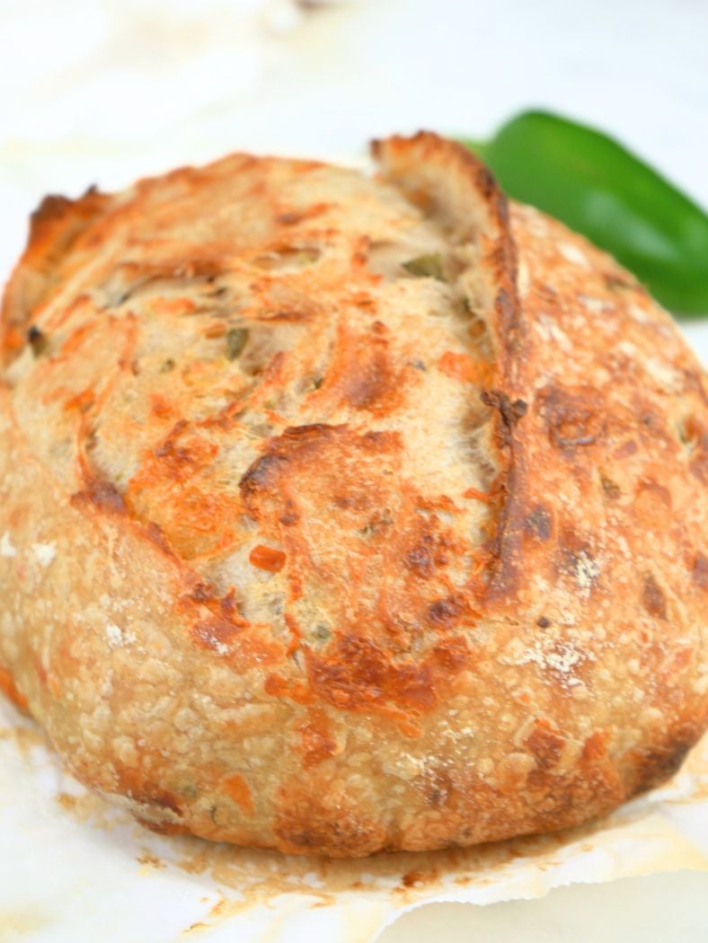 A boule of sourdough cheddar jalapeño bread resting on parchment paper