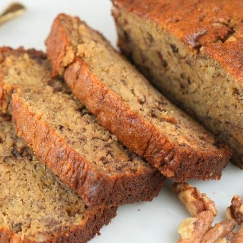 A loaf of sourdough discard banana bread sliced and next to walnuts and a gold knife