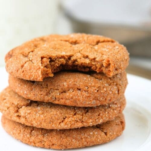 Stack of chewy sourdough ginger molasses cookies with a bite taken out on a white plate.