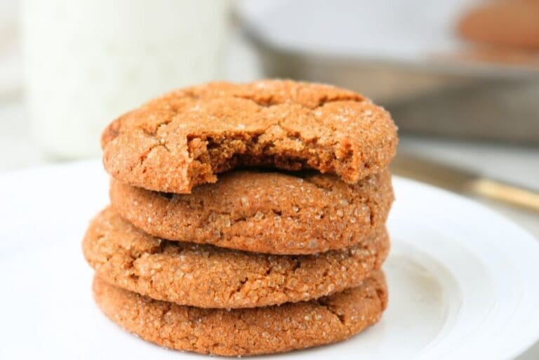 Stack of chewy sourdough ginger molasses cookies with a bite taken out on a white plate.