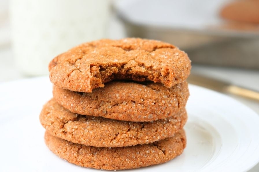 Stack of chewy sourdough ginger molasses cookies with a bite taken out on a white plate.