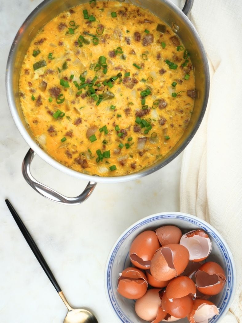 Overhead of finished slow cooker breakfast casserole, shown with a serving spoon and a bowl of cracked egg shells