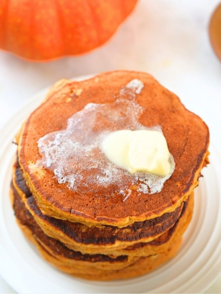 An overhead view of a stack of pumpkin spice pancakes with butter melting on top
