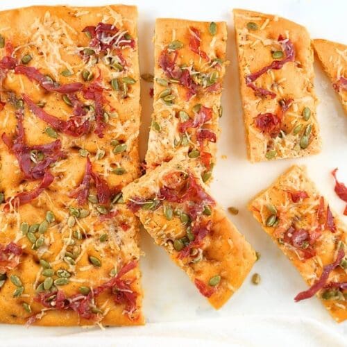 Pumpkin sourdough focaccia with slices scattered on a counter.