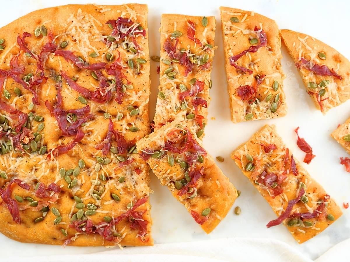 Pumpkin sourdough focaccia with slices scattered on a counter.