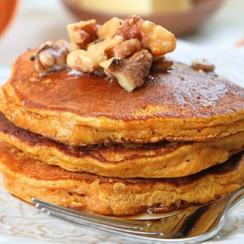 A stack of pumpkin spice pancakes on a plate, topped with walnut and syrup.