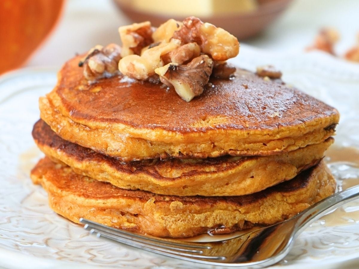 A stack of pumpkin spice pancakes on a plate, topped with walnut and syrup.