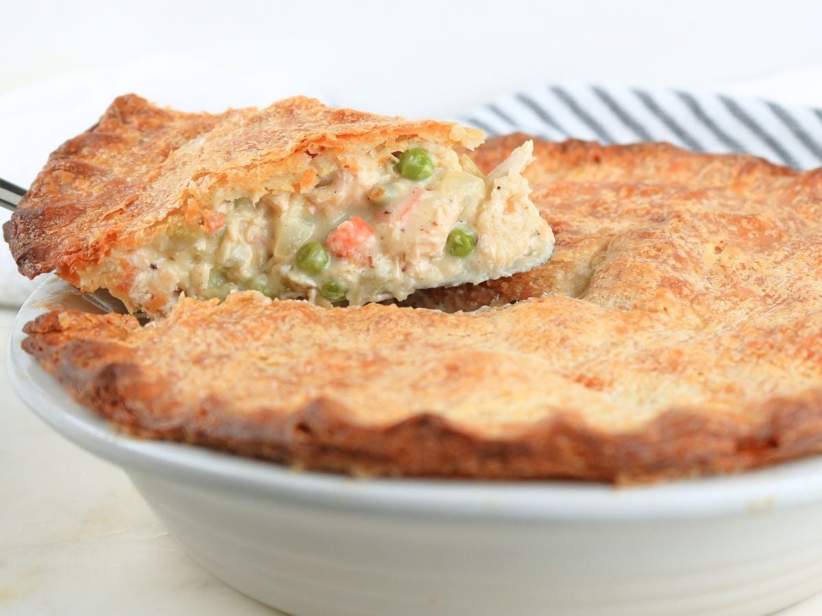 A slice of sourdough chicken pot pie on a pie server being lifted from a pie dish.