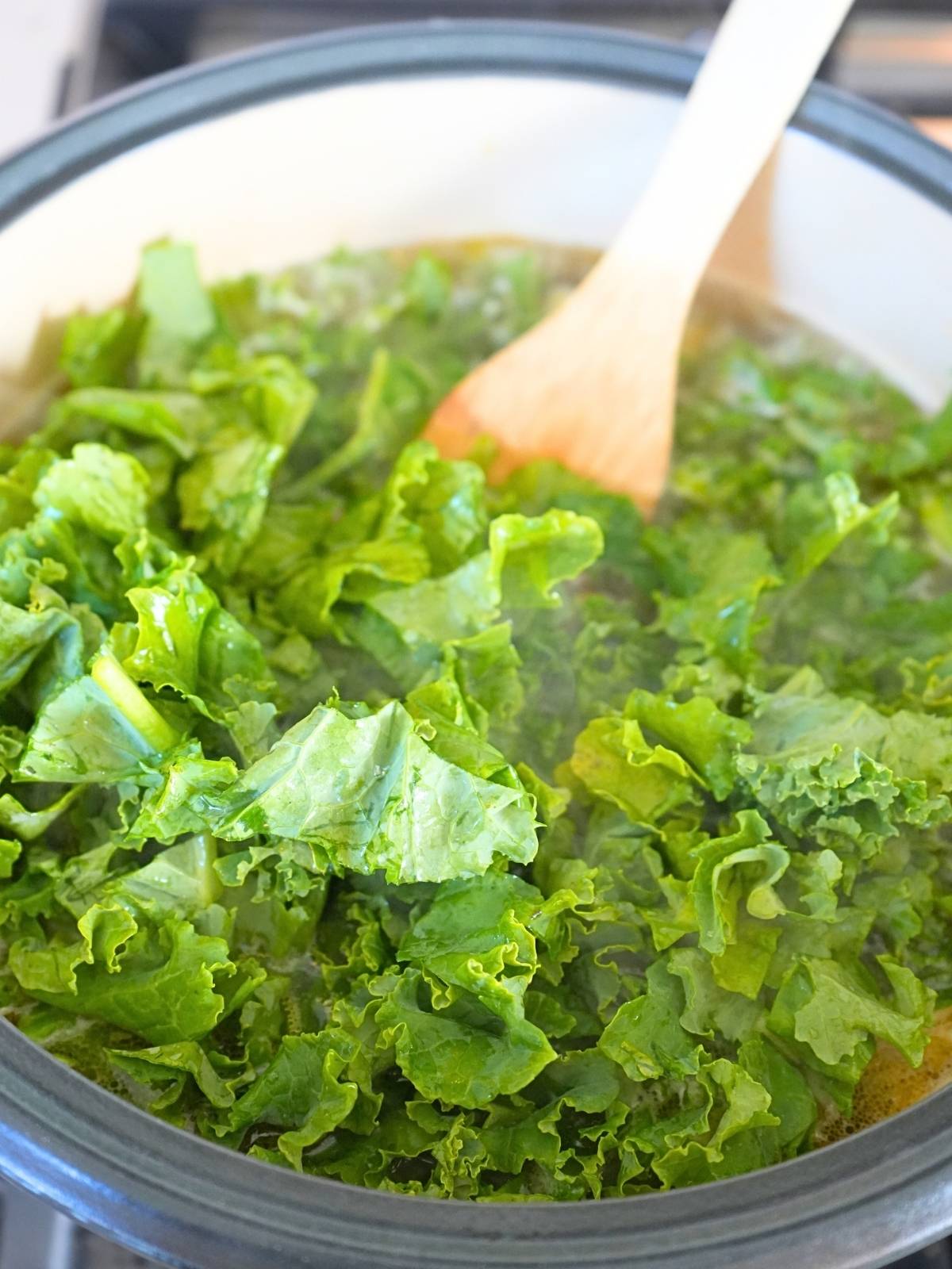 Chopped kale in a Dutch oven, being stirred into soup.