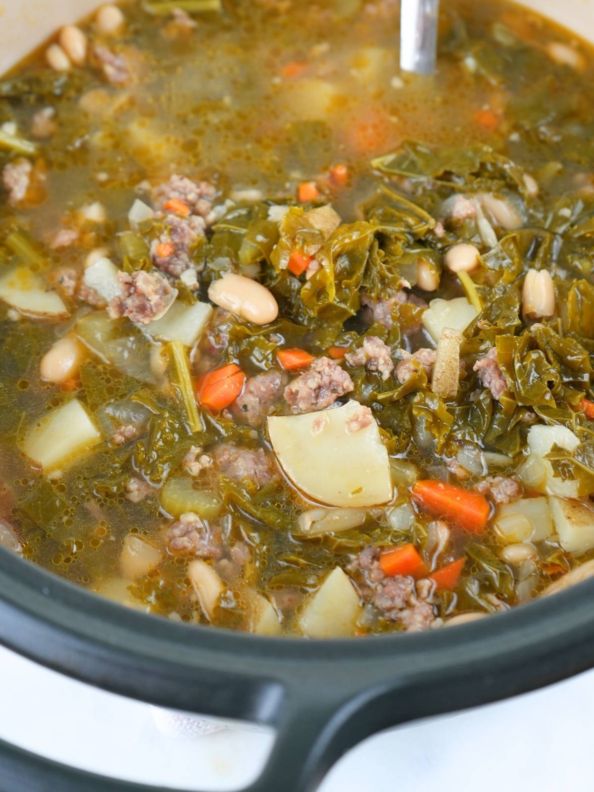 A Dutch oven filled with sausage, kale, and white bean soup.