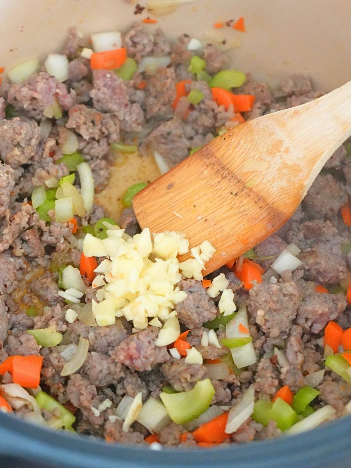 Minced garlic added to meat mixture in a Dutch oven.