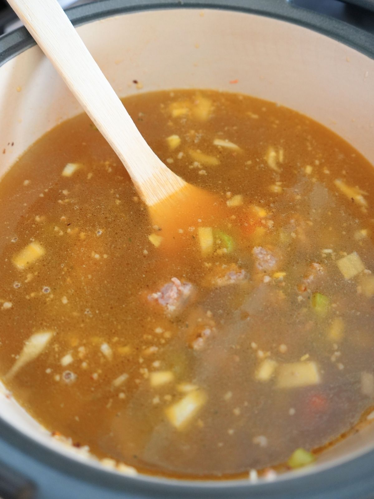 Broth poured into a large Dutch oven, shown with wood spatula