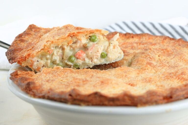 A slice of pot pie on a pie server being lifted from the pie dish