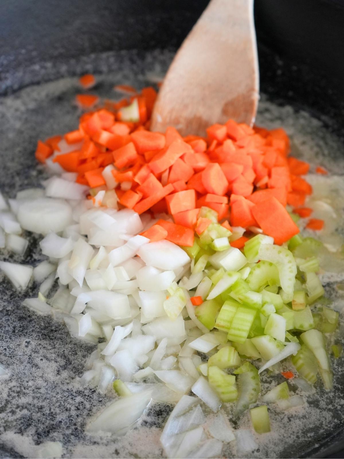 Chopped carrots, celery, and onions being sautéed in a cast iron skillet.
