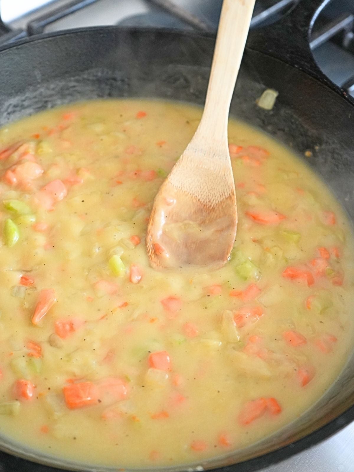 Pot pie filling in a skillet, shown with a wooden spoon.