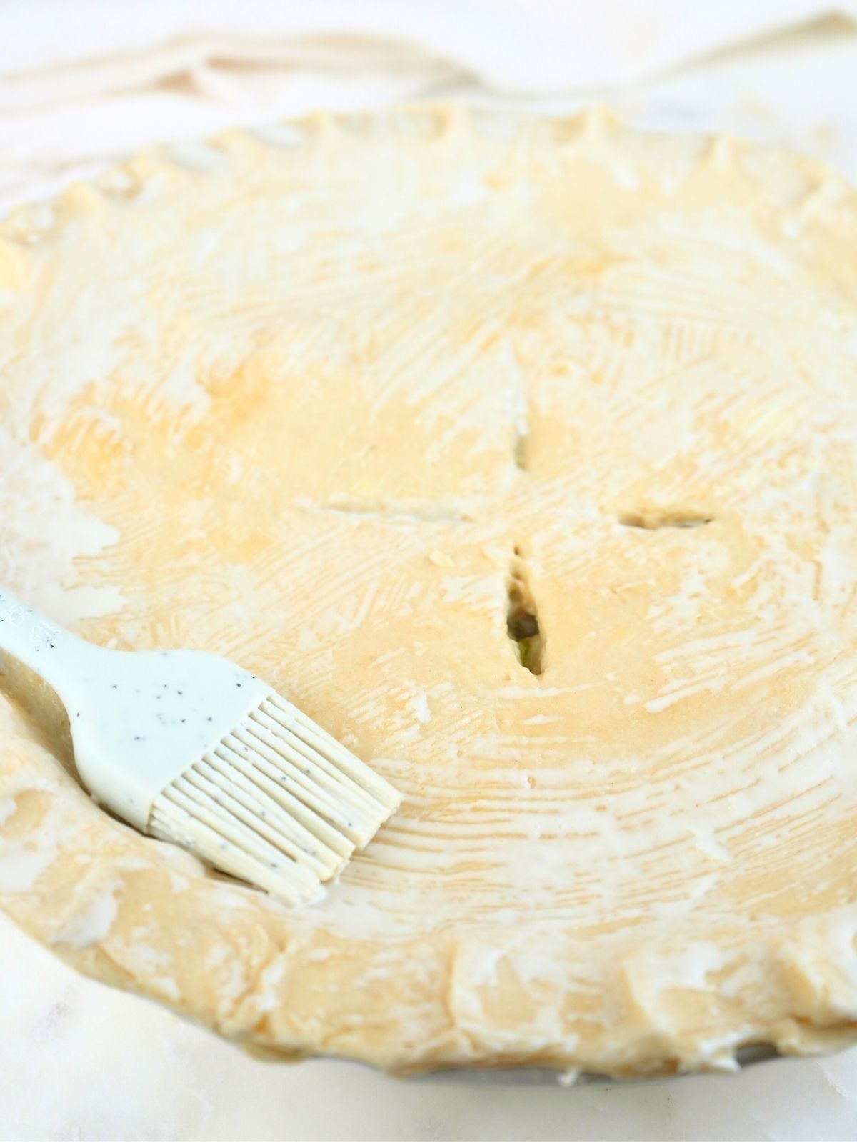 A pie brushed with heavy cream, shown with a silicone pastry brush.