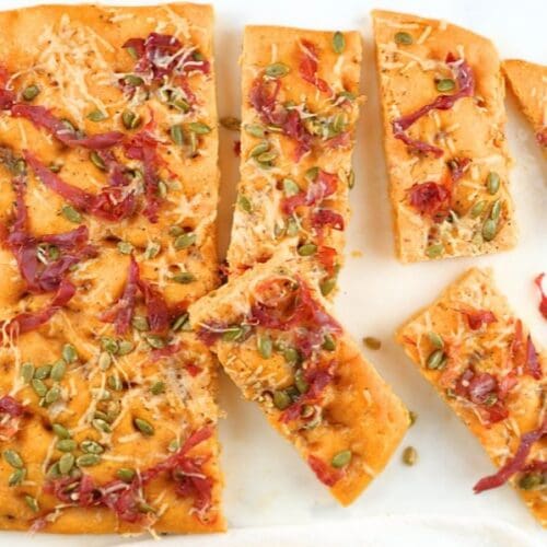 An overhead view of pumpkin sourdough focaccia with slices scattered on a white counter