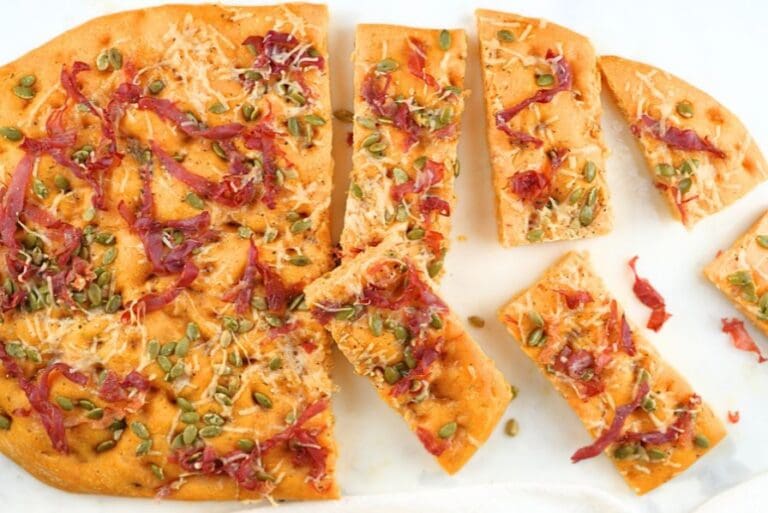 An overhead view of pumpkin sourdough focaccia with slices scattered on a white counter
