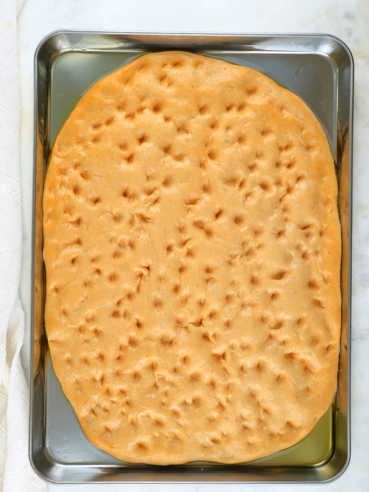 Pumpkin sourdough focaccia dough dimpled on a baking sheet,