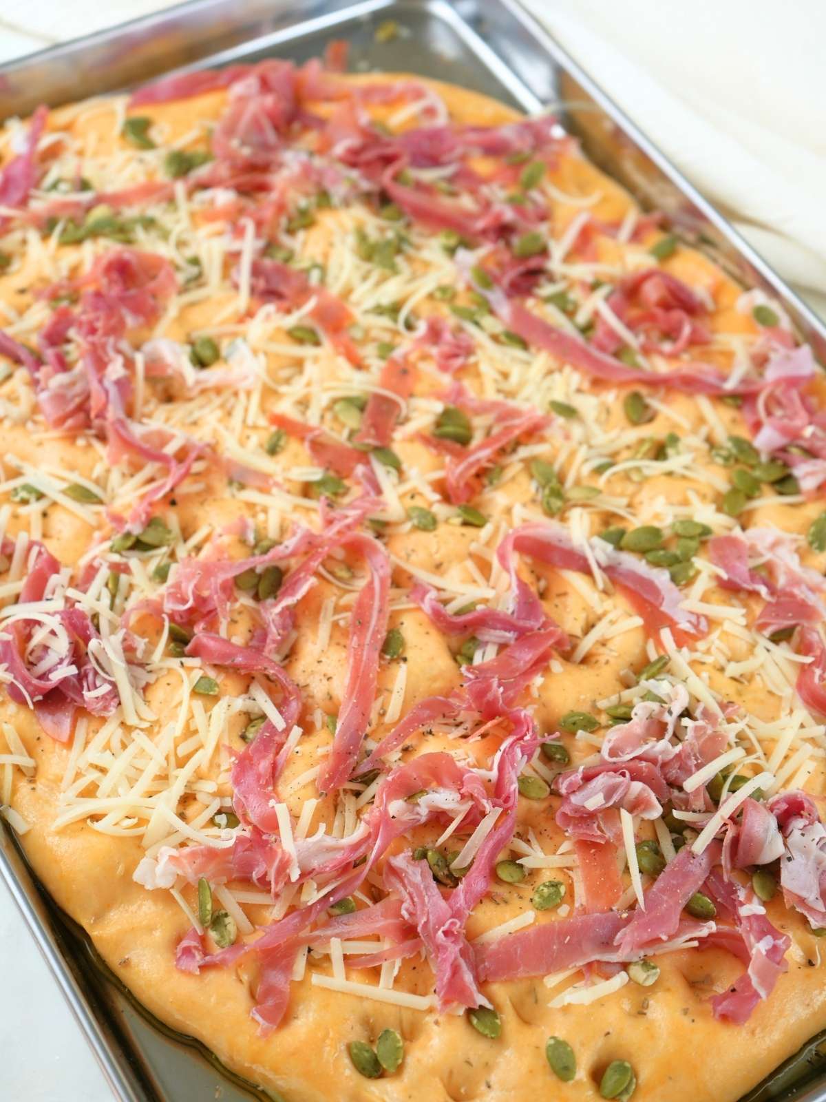 Sourdough pumpkin focaccia topped with prosciutto on a baking sheet.
