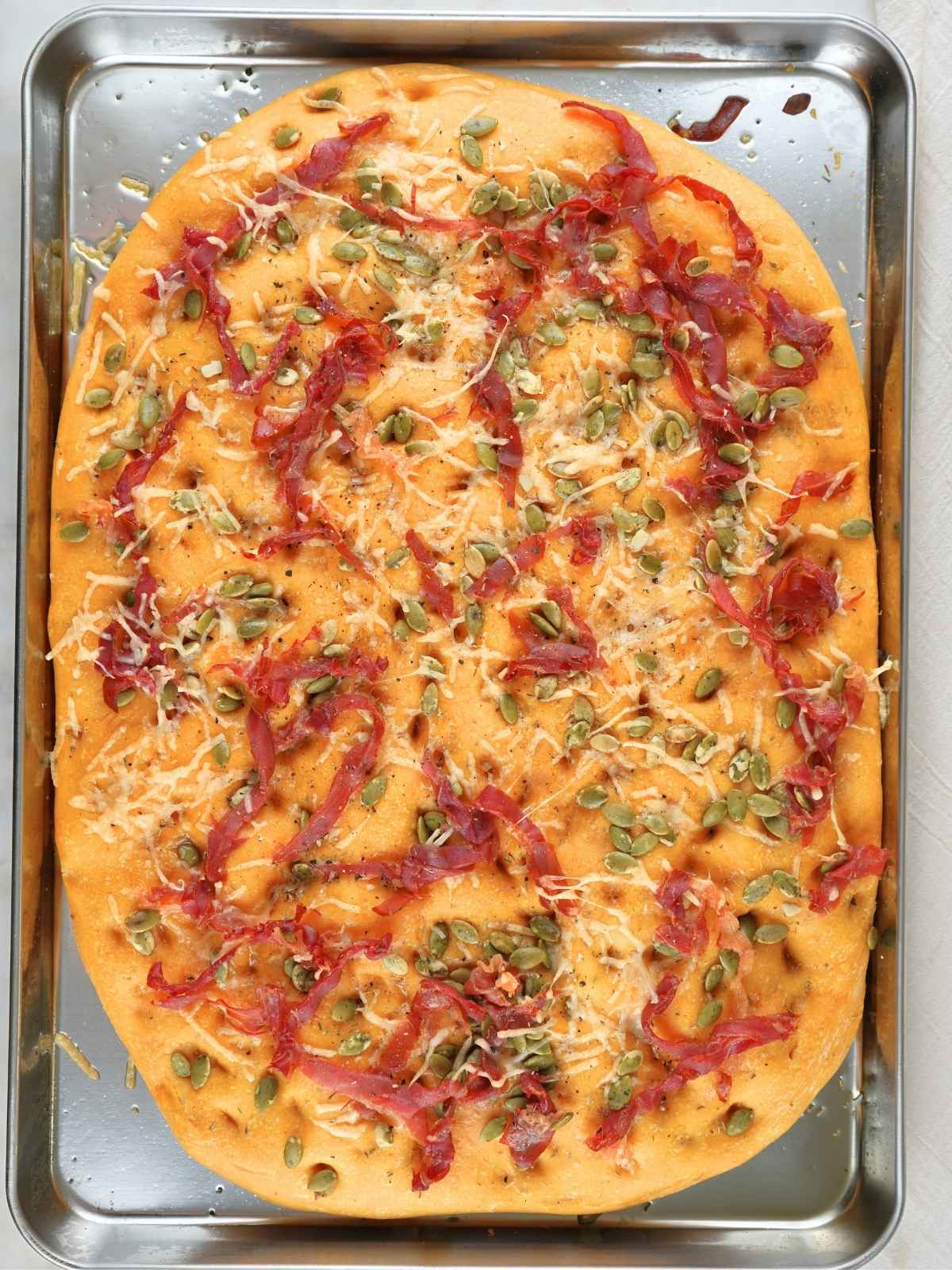 Baked sourdough pumpkin prosciutto focaccia on a baking sheet.