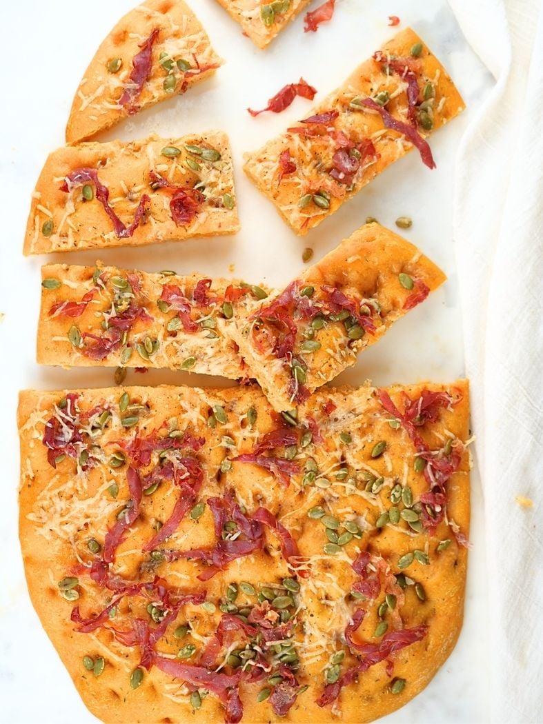 A overhead of sourdough pumpkin prosciutto focaccia, half sliced into pieces and scattered