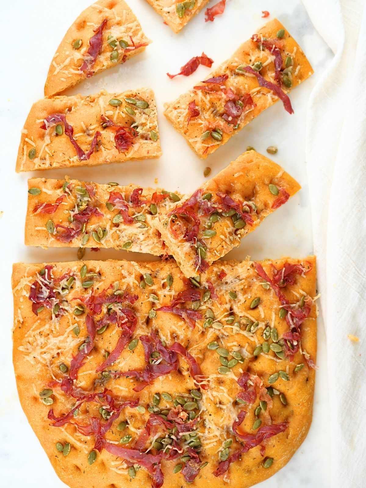 Sourdough pumpkin prosciutto focaccia, half sliced into pieces and scattered.