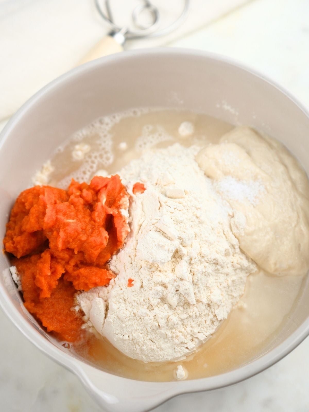 A mixing bowl with ingredients for making pumpkin dough in it.