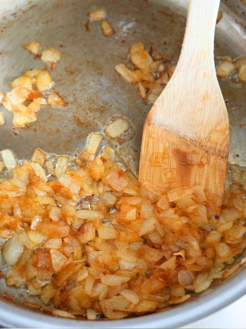 Caramelized chopped onions in a skillet with a wooden spatula