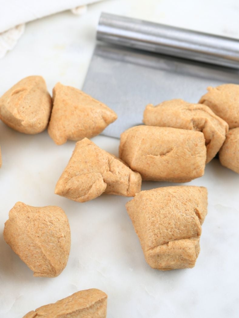 Dough divided into small portions, shown with a bench scraper