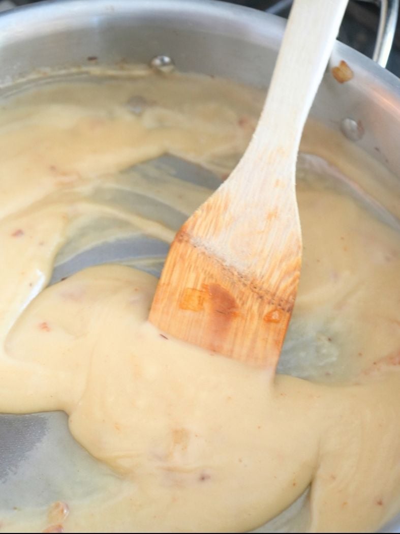 A creamy roux in a skillet with a wooden spatula