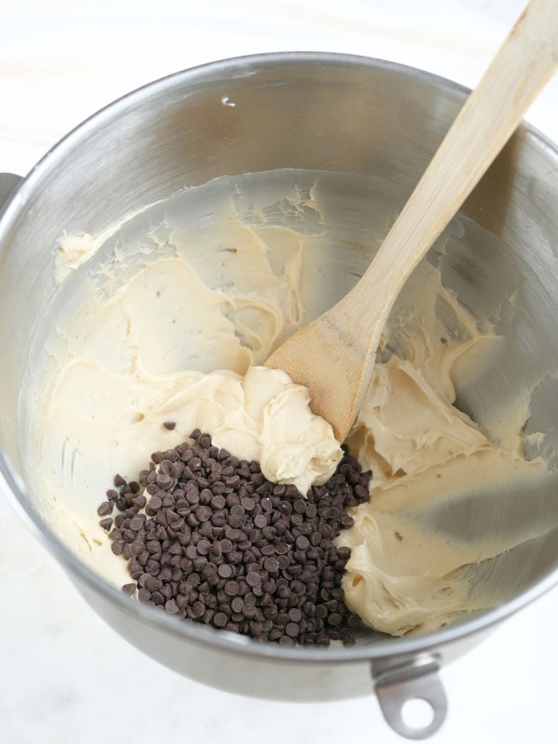 Cheese ball mixture with mini chocolate chips on top, shown with in a mixing bowl with wooden spoon